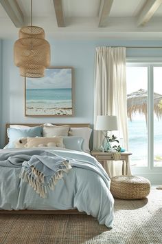 a bedroom with blue walls and white bedding in front of a large window overlooking the ocean