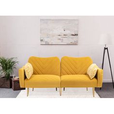 a yellow couch sitting on top of a white rug next to a lamp and potted plant