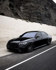 a black car parked on the side of a road next to a mountain covered in snow