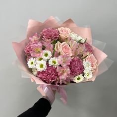 a bouquet of pink and white flowers is held by a person's hand on a gray background