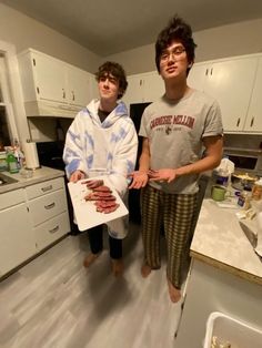 two young men standing in a kitchen holding food