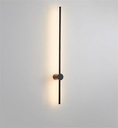 a wall mounted light on the side of a white wall next to a black pole