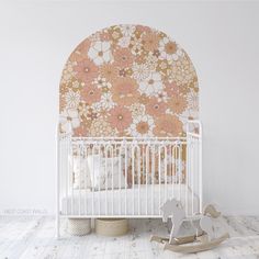 a white crib in front of a floral wallpaper with a rocking horse next to it