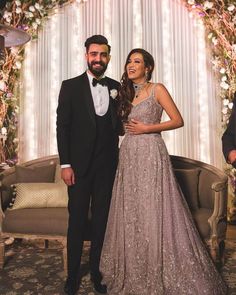 a man and woman standing next to each other in front of a floral arch with lights