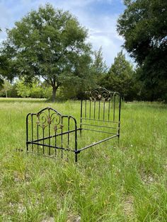 an old iron bed frame sitting in the middle of a grassy field with trees behind it