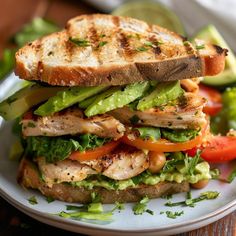 a grilled chicken sandwich with lettuce, tomato and cucumber on a plate