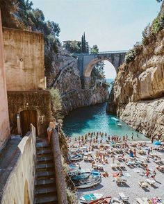 many people are laying on the beach in front of an old stone bridge and pool