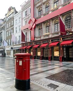 a red post box sitting on the side of a street next to tall buildings with awnings