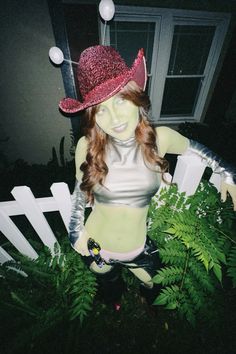 a woman with long hair wearing a pink hat and white top standing in front of a fence