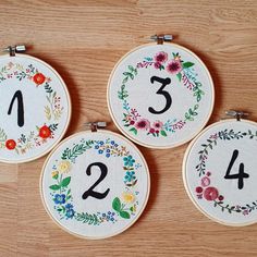 three cross stitch hoops with numbers and flowers on them sitting on a wooden surface