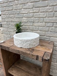 a white sink sitting on top of a wooden table next to a brick wall and potted plant