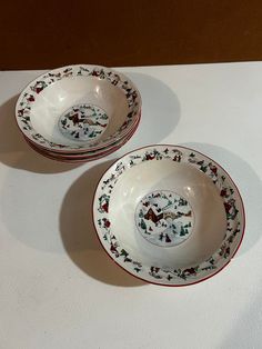 two white bowls sitting on top of a table with red trimmings and holly decorations