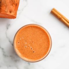 a glass filled with liquid next to two cinnamon sticks on a white tablecloth and marble counter top