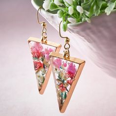 a pair of triangle shaped earrings with flowers on them sitting next to a potted plant