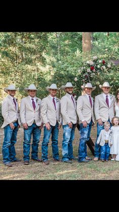 a group of people standing next to each other in front of trees and grass with one person wearing a cowboy hat