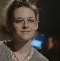 a woman wearing glasses and a necklace in front of her face is looking at the camera