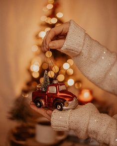 a person holding a christmas ornament in front of a small tree with lights