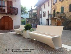 two white benches sitting next to each other on a cobblestone street with buildings in the background