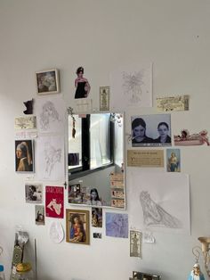 a white wall covered in pictures and drawings on it's side with a mirror