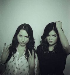 two women standing next to each other in front of a white wall with their hands up