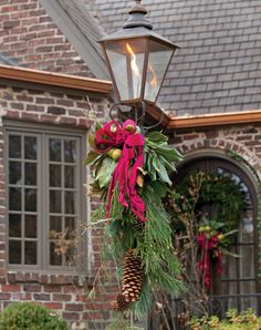 a christmas wreath hanging from a lamp post in front of a brick house with red bows and pine cones