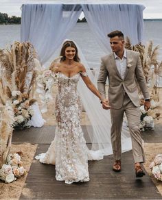 a bride and groom holding hands walking down the aisle to their wedding ceremony by the water