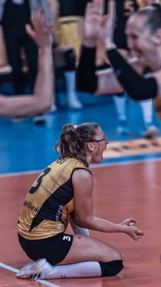 a female volleyball player kneeling down on the floor with her hands up in the air