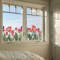 a bed sitting under two large windows next to a window sill with flowers painted on it