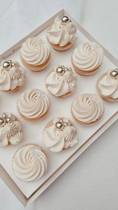 twelve cupcakes with white frosting in a box on top of a table