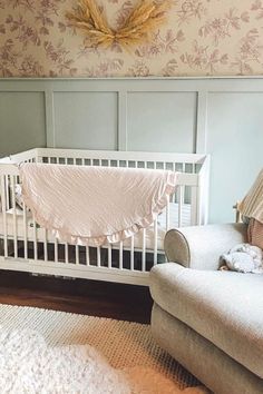 a baby crib in a room with floral wallpaper on the walls and a white chair