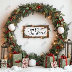 a christmas wreath with presents and lights on the wall in front of it that says joy to the world