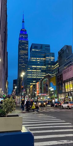 a city street filled with lots of traffic next to tall buildings at night, and people crossing the street