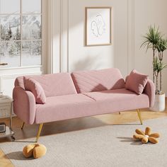 a pink couch sitting on top of a wooden floor next to a potted plant