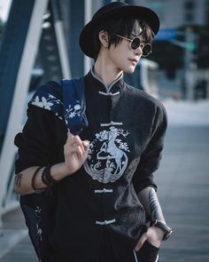 a young man wearing sunglasses and a black hat walks down the street with his hand in his pocket