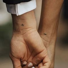 two people holding hands with small tattoos on their wrists, one is black and the other is white