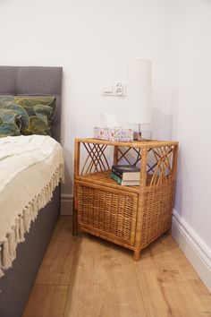 a wicker basket sitting on top of a bed next to a night stand with a pillow