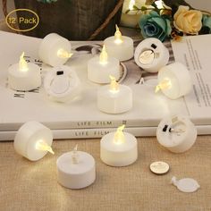 some white candles sitting on top of a book next to flowers and other things that are lit up