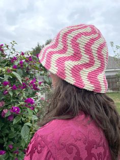 a woman wearing a pink and white crocheted hat looking at flowers in the background