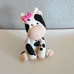 a toy cow with a pink bow sitting on top of a white table next to a wall