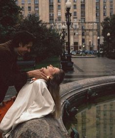 a woman laying on top of a rock next to a man in a black suit