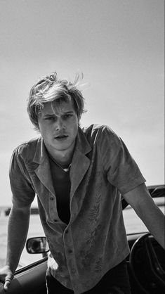 a young man leaning on the hood of a car