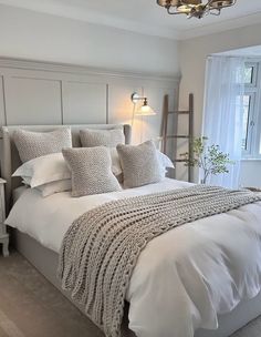 a bed with white linens and pillows in a bedroom next to a large window