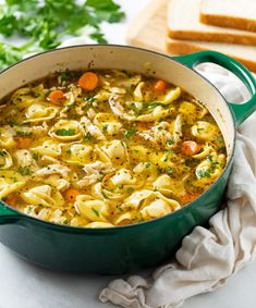 a green pot filled with chicken noodle soup on top of a white counter next to slices of bread