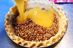 a person pouring orange juice into a pie crust filled with nuts and other food items