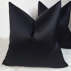 two black pillows sitting on top of a white furnishing floor next to each other