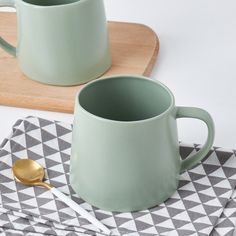 two green mugs sitting next to each other on top of a wooden cutting board