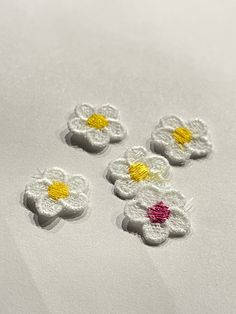 four small white flowers with yellow centers sitting on top of a sheet of paper next to each other