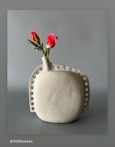 a white vase with flowers in it on a gray tableclothed surface and grey background