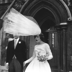 a man and woman dressed in formal wear holding hands while walking down the street with an umbrella over their heads