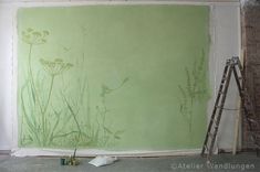 a green wall with flowers painted on it and a ladder leaning up against the wall